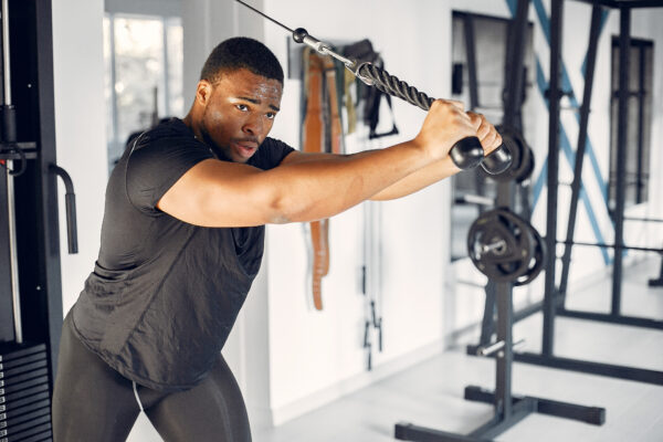 Sports man in the gym. A black man performs exercises. Guy in a black t-shirt